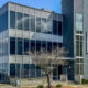 Modern glass office building with reflective windows and a tall vertical facade labeled '615 Building' against a blue sky.