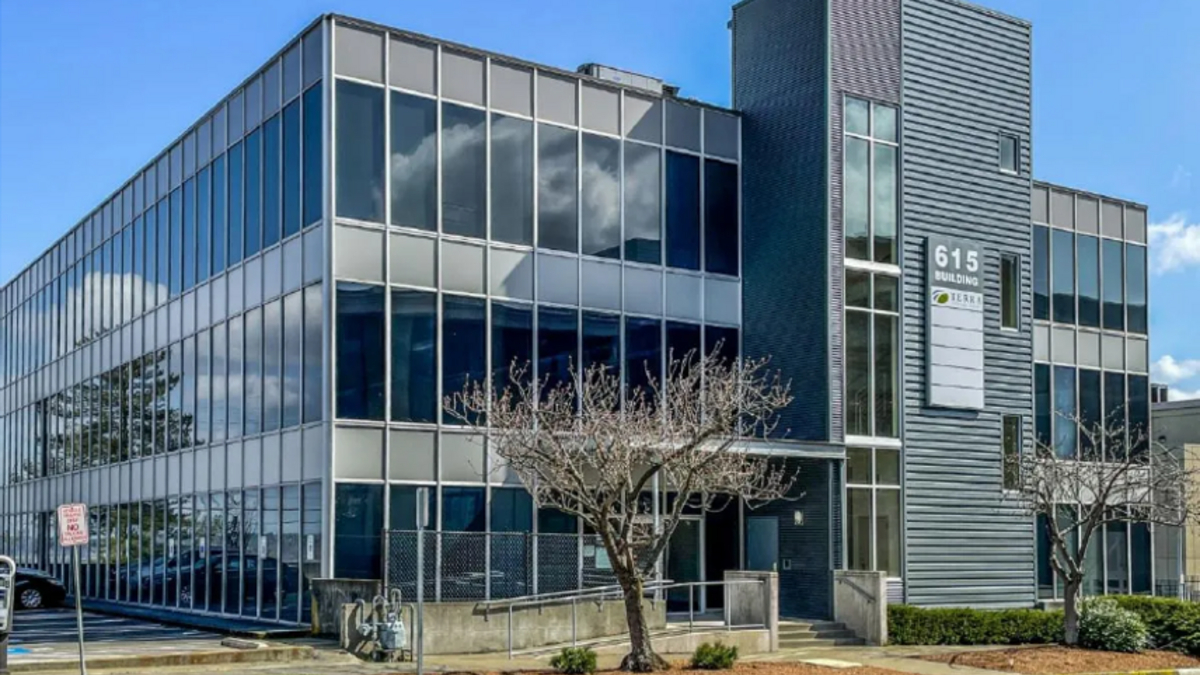 Modern glass office building with reflective windows and a tall vertical facade labeled '615 Building' against a blue sky.