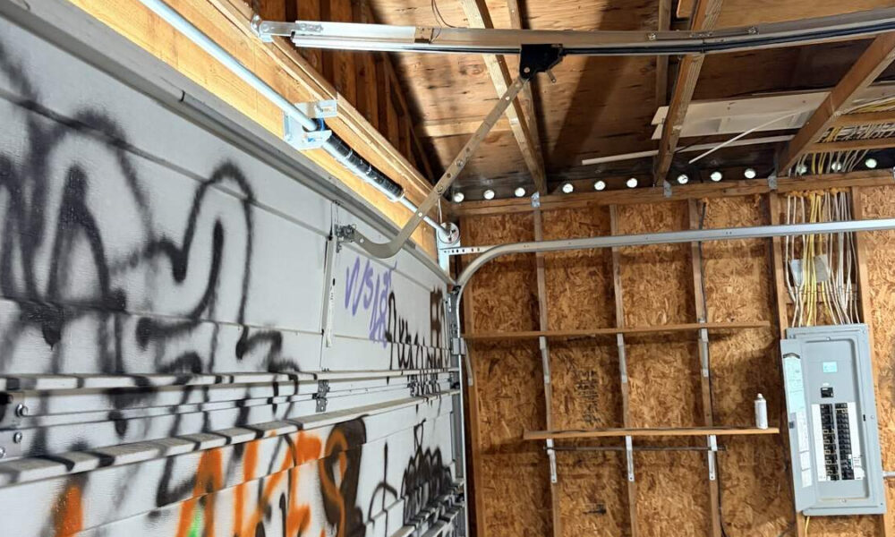Graffiti-tagged garage door inside a shed with exposed plywood walls and an electrical panel visible to the right.