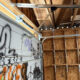 Graffiti-tagged garage door inside a shed with exposed plywood walls and an electrical panel visible to the right.