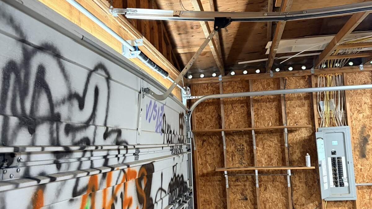 Graffiti-tagged garage door inside a shed with exposed plywood walls and an electrical panel visible to the right.