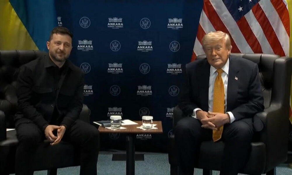 Two men sit in leather chairs at a formal meeting, with Ankara backdrop and US flag behind them.