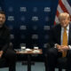Two men sit in leather chairs at a formal meeting, with Ankara backdrop and US flag behind them.