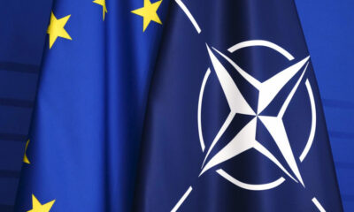 Close-up of blue flags featuring the NATO emblem and partial European Union stars on the left.