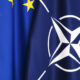Close-up of blue flags featuring the NATO emblem and partial European Union stars on the left.