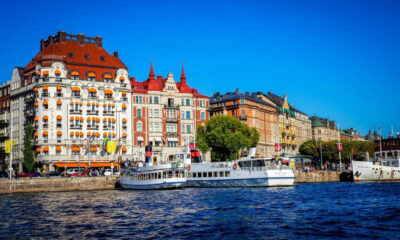 Colorful historic buildings with orange awnings line the harbor as white passenger boats sail by under a blue sky.