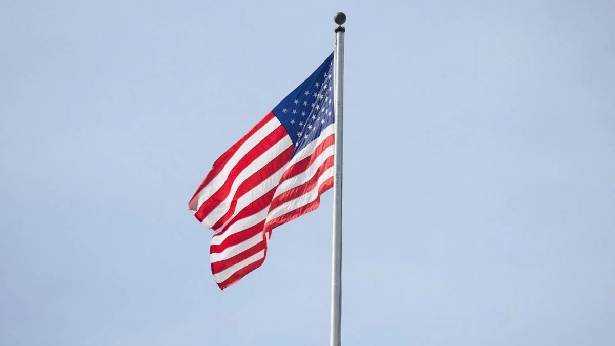 American flag fluttering on a tall flagpole against a clear blue sky.