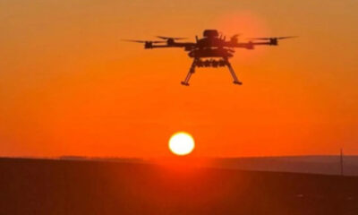 Quadcopter drone hovering at sunset over a flat landscape with an orange sky.