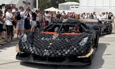 Exotic black sports car wrapped in circular panels on display, surrounded by a crowd of photographers and onlookers.
