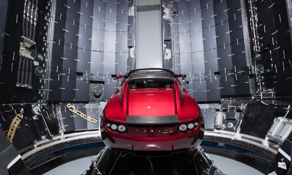 Red sports car in a circular wind-tunnel testing chamber with panels and sensors around it, showcasing aerodynamic testing setup.
