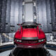 Red sports car in a circular wind-tunnel testing chamber with panels and sensors around it, showcasing aerodynamic testing setup.