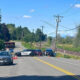 Police cars block a rural two-lane road with orange cones; railroad tracks and trees in the background.