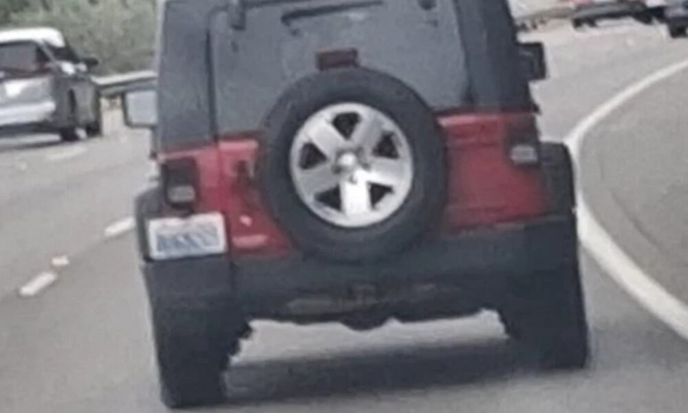 Rear view of a black SUV with a spare tire mounted on the back, driving on a curved highway road.