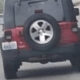 Rear view of a black SUV with a spare tire mounted on the back, driving on a curved highway road.