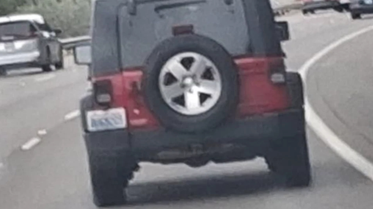 Rear view of a black SUV with a spare tire mounted on the back, driving on a curved highway road.