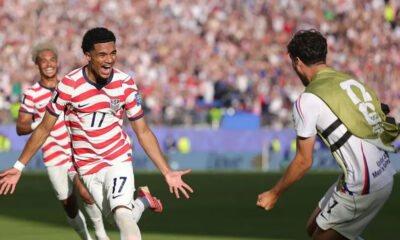 USA soccer player wearing number 17 celebrates with arms outstretched as fans cheer in a full stadium.