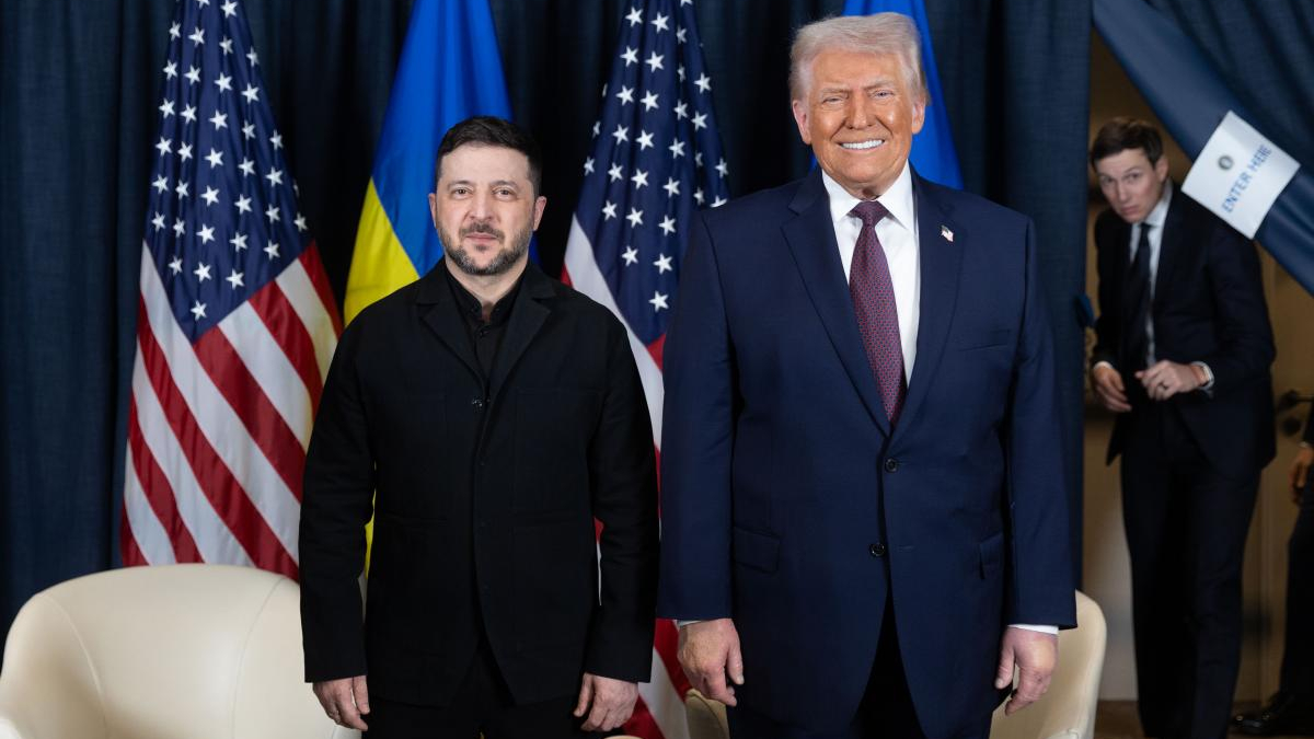 Ukrainian President Zelenskyy and former President Trump pose for a photo at a formal event with US and Ukrainian flags behind them.