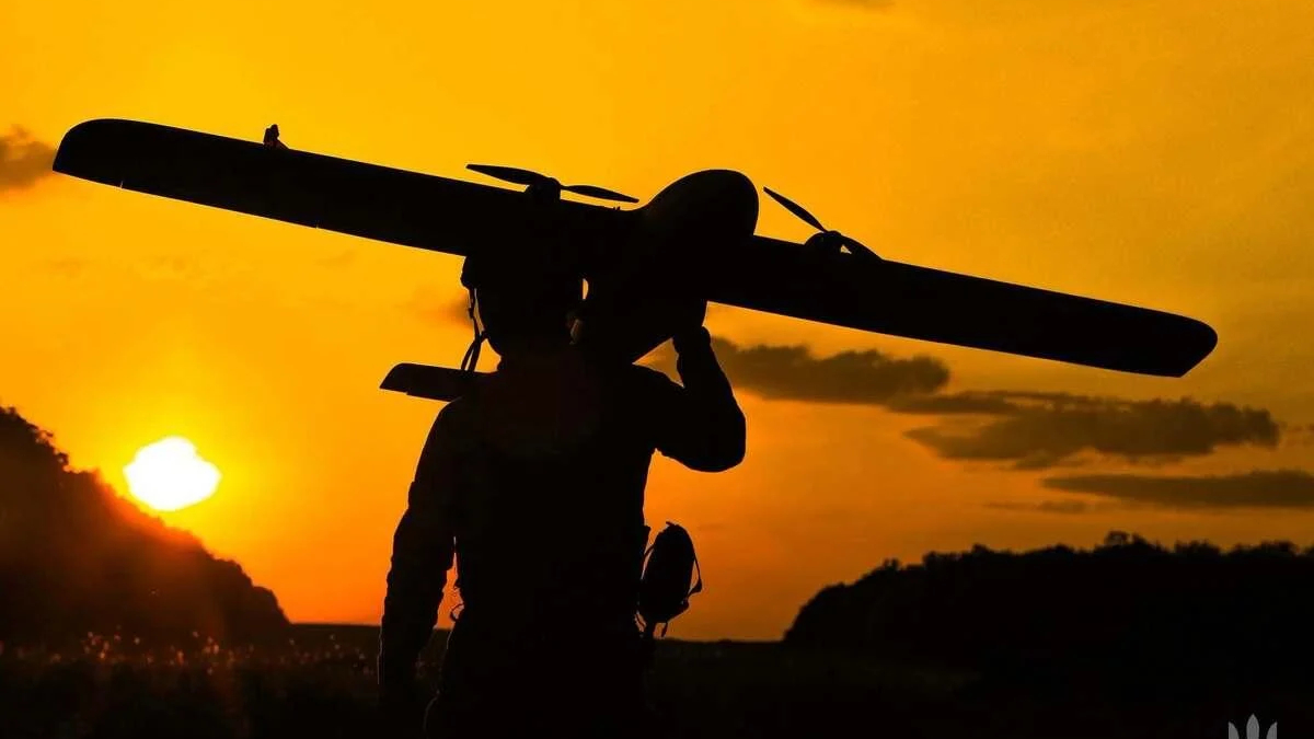 Silhouette of a person carrying a small propeller plane over their shoulder at sunset, orange sky in the background.