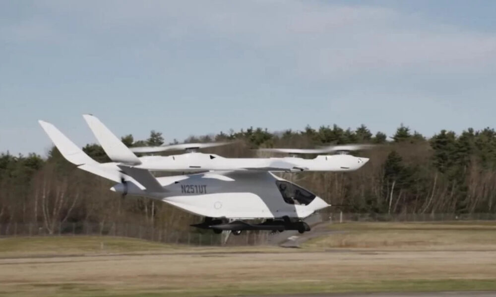 White tilt-rotor aircraft lifting off from a runway, with dual wing-mounted rotors and a compact cockpit.