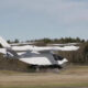 White tilt-rotor aircraft lifting off from a runway, with dual wing-mounted rotors and a compact cockpit.