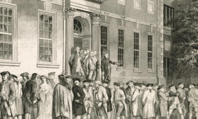 Historic crowd gathered outside a grand neoclassical building with tall columns and arched entrance.