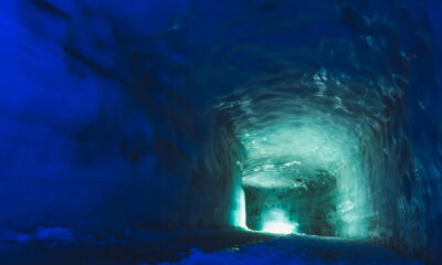 Ice cave tunnel with blue ice walls and a turquoise glow at the far end of the tunnel.