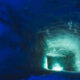 Ice cave tunnel with blue ice walls and a turquoise glow at the far end of the tunnel.