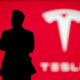 Silhouette of a person in front of a red background with the blurred Tesla logo, suggesting a Tesla executive or spokesperson.