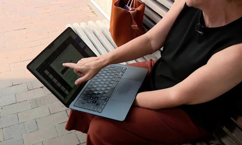 Person sitting on a bench outdoors, pointing at text on a laptop screen.
