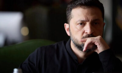 Man with dark hair and beard resting his chin on his hand, looking thoughtful.