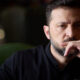 Man with dark hair and beard resting his chin on his hand, looking thoughtful.