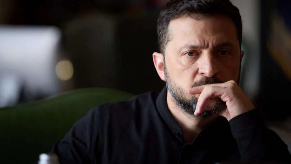 Man with dark hair and beard resting his chin on his hand, looking thoughtful.
