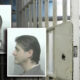 Mugshots of a man (front and side profiles) displayed against a jail cell background with bars in view behind them.