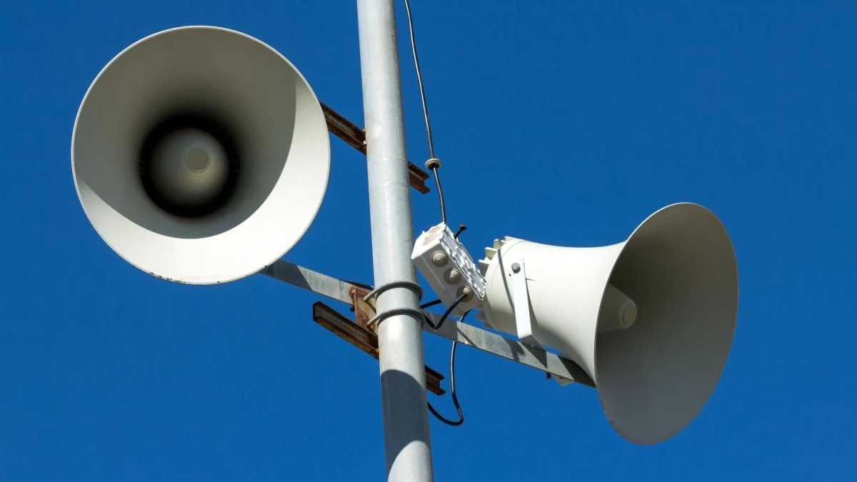 Public address speakers mounted on a metal pole against a clear blue sky.