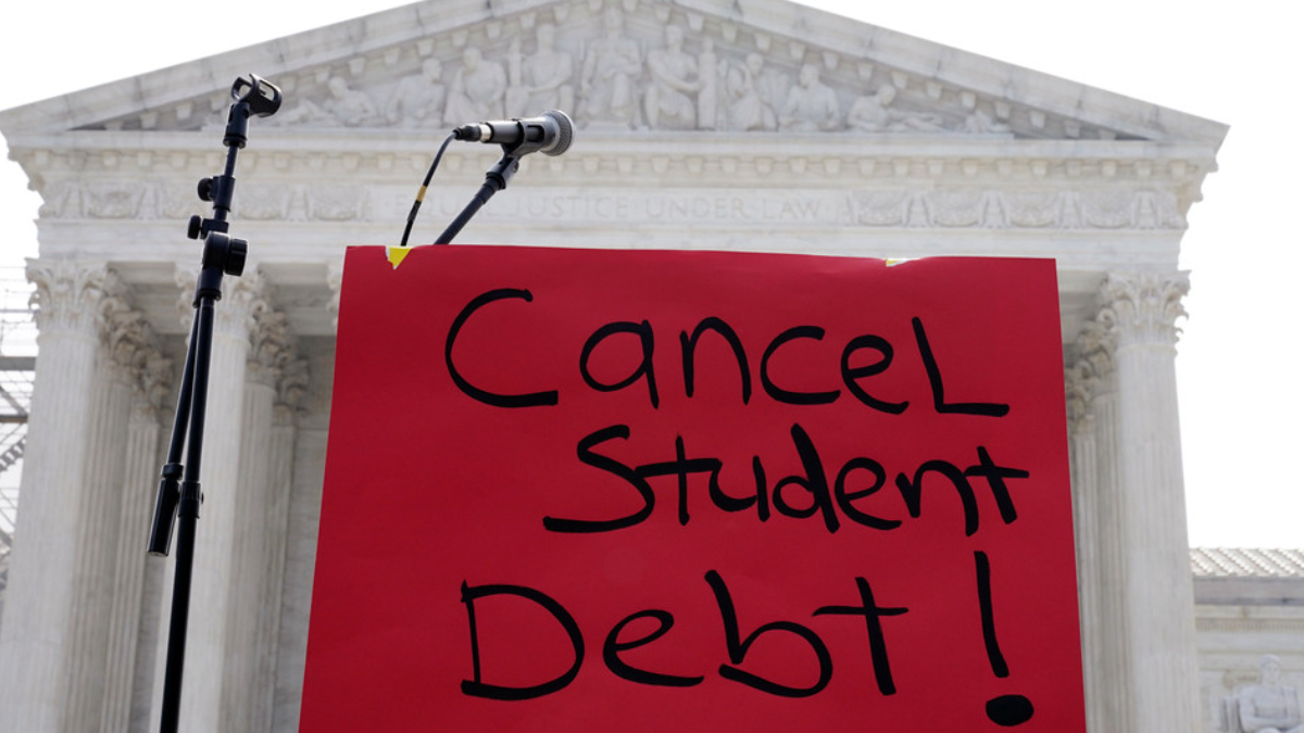 Red protest sign reading 'Cancel Student Debt!' with microphones in front of a classical courthouse backdrop.