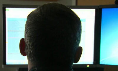 Back of a person's head facing two computer monitors with bright screens in an office setting