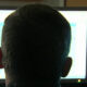 Back of a person's head facing two computer monitors with bright screens in an office setting