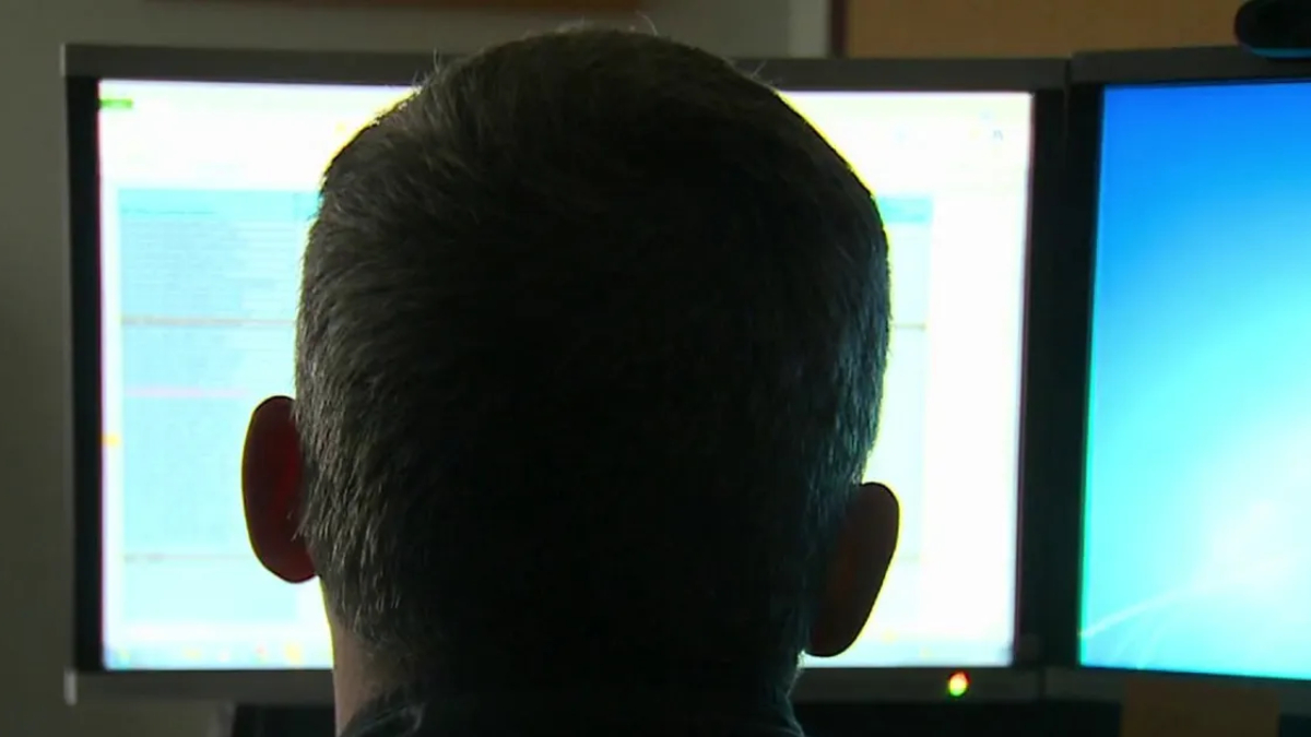 Back of a person's head facing two computer monitors with bright screens in an office setting