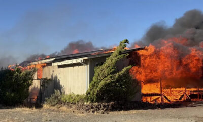 A single-story shed engulfed in flames with thick black smoke rising above it.