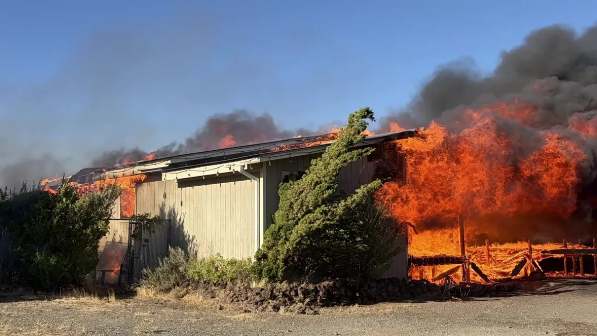 A single-story shed engulfed in flames with thick black smoke rising above it.