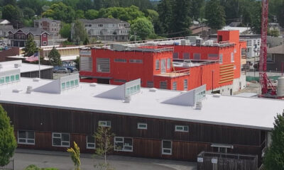 Orange, multi-story building under construction beside a dark brown low-rise, with a red construction crane nearby.