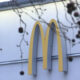 McDonald's golden arches logo on the side of a building, with tree branches in the foreground outside a fast-food restaurant