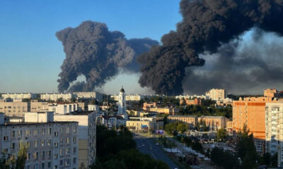 City skyline with huge black smoke plumes rising from distant fires near a church steeple
