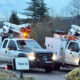 Two white utility trucks with bucket lifts parked side by side in a driveway, orange warning lights flashing on top, with a small 'Thank You' sign in the foreground.