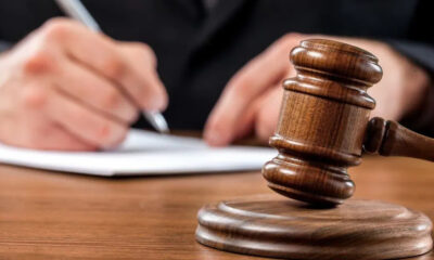 Wooden judge's gavel resting on a sound block with a person signing a document in the background.
