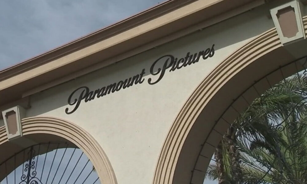 Paramount Pictures sign on a cream building with decorative arches and wrought-iron gates, palm trees nearby