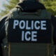 Back view of a law enforcement officer wearing a tactical vest with a 'POLICE ICE' patch.