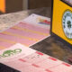 Close-up of pink and white lottery tickets laid out on a dark countertop beside a yellow lottery sign.