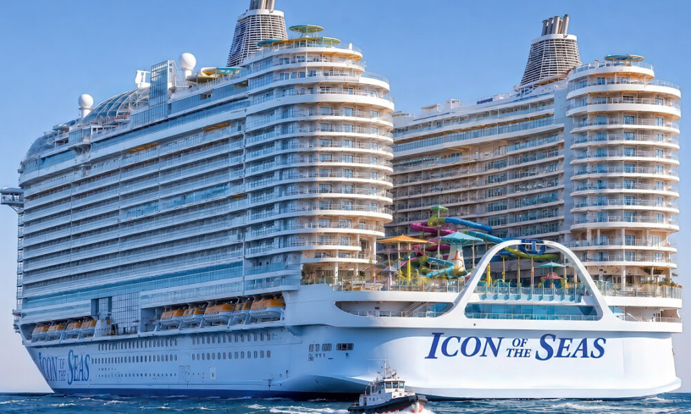 Large white cruise ship with colorful water slides on top, labeled Icon of the Seas, sailing on calm blue water with a small tender nearby