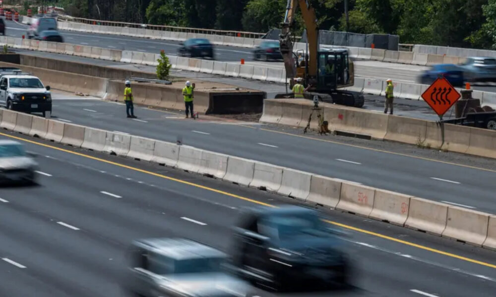 Highway construction zone with workers in reflective vests, concrete barriers, and an excavator at work near a split in traffic.